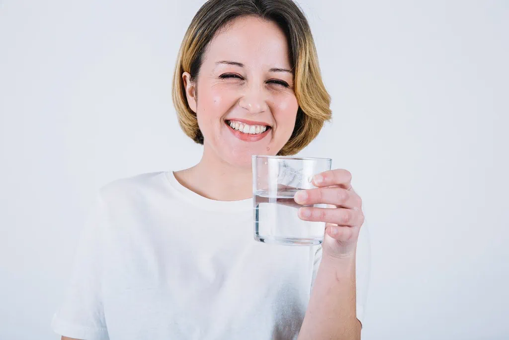 Smiling woman with short hair and white t-shirt holding a glass of water.