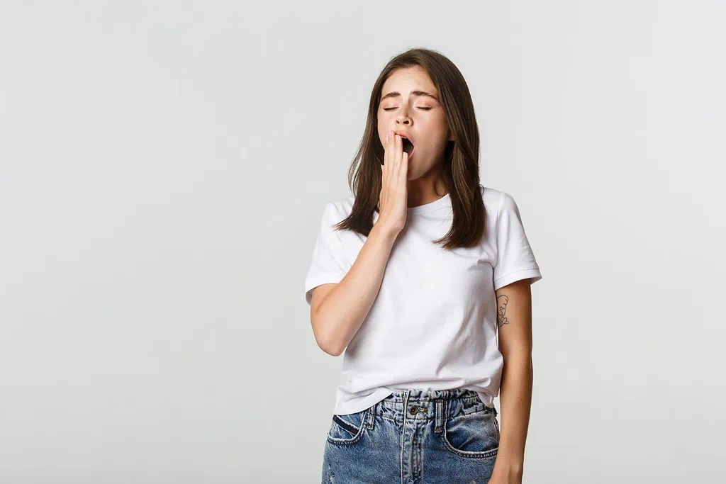 Young woman yawning, covering her mouth, wearing white t-shirt and jeans