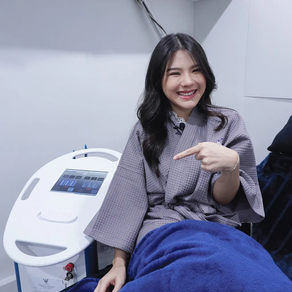 Smiling woman in robe pointing at CRISTAL aesthetic body contouring device.