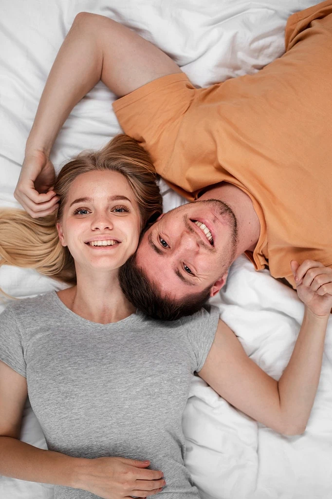 Smiling young couple lying on a white bed, seen from an overhead view